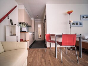 A compact living space with a kitchenette, a dining area with red chairs, a sofa, and a bedside table with a lamp. - Paradies 606 Appartement/Fewo, Bad, WC, 2-Bettwohnung by Interhome (Arosa)