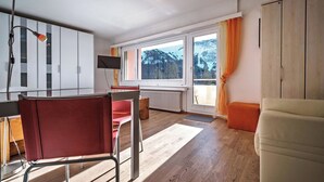 Una sala moderna con piso de madera, un sillón rojo, un sofá blanco, un televisor y una ventana con vistas a montañas.