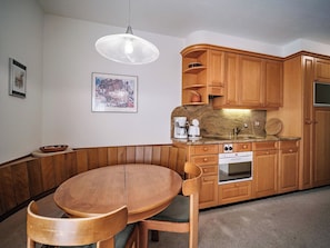 A kitchen with wooden cabinets, a built-in oven, and a round dining table with chairs. - Paradies 506 Appartement/Fewo,  , 2-Bettwohnung 2-Bettwohnung by Interhome (Arosa)