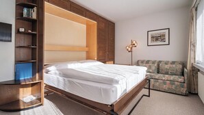 Un dormitorio con cama, armario, escritorio, silla y lámpara de pie.