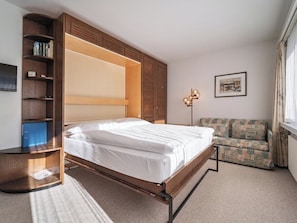 A bedroom with a bed, a wardrobe, a desk, a chair, and a floor lamp. - Paradies 506 Appartement/Fewo,  , 2-Bettwohnung 2-Bettwohnung by Interhome (Arosa)