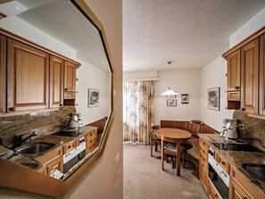 A compact kitchen with wooden cabinets, a built-in oven, and a dining area with a table and chairs. - Paradies 506 Appartement/Fewo, Dusche, WC, 2-Bettwohnung 2-Bettwohnung by Interhome (Arosa)