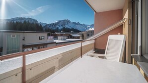 Un balcón con vista a montañas nevadas, baranda de madera y una mesa.