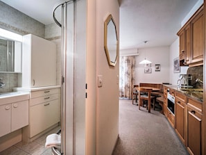 A modern kitchen with wooden cabinets, a dining area with a bench, and a glass shower enclosure. - Paradies 506 Appartement/Fewo, Dusche, WC, 2-Bettwohnung 2-Bettwohnung by Interhome (Arosa)