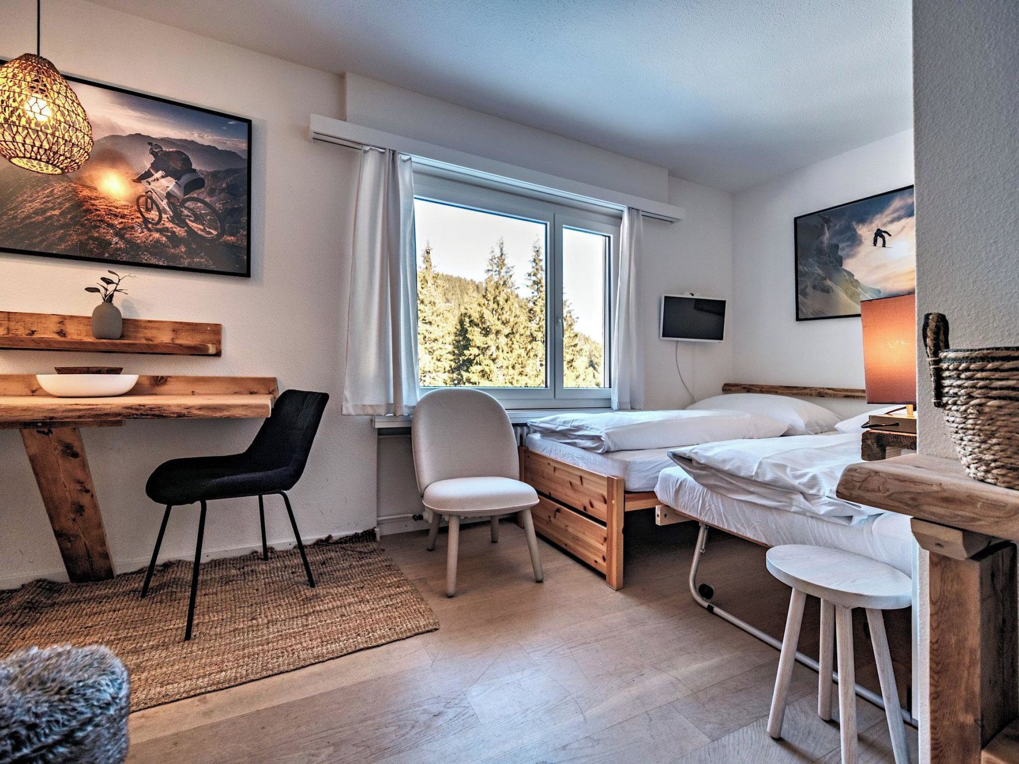 Une chambre à coucher comprenant un lit, un bureau, une chaise, une fenêtre donnant sur des arbres et un téléviseur fixé au mur.