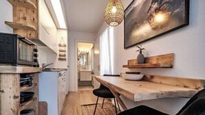 Eine kleine Küche mit Mikrowelle, Holzregalen, einer Hängeleuchte und einem Essbereich mit Tisch und Stühlen.