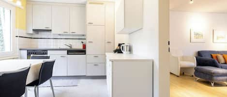 Una cocina moderna con armarios blancos, un comedor con mesa y sillas, y una sala de estar con sofá.