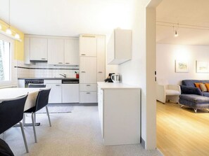 A modern kitchen with white cabinets, a dining area with a table and chairs, and a living room with a sofa. - Paradies 021 Appartement/Fewo, Bad, WC, 4-Bettwohnung by Interhome (Arosa)