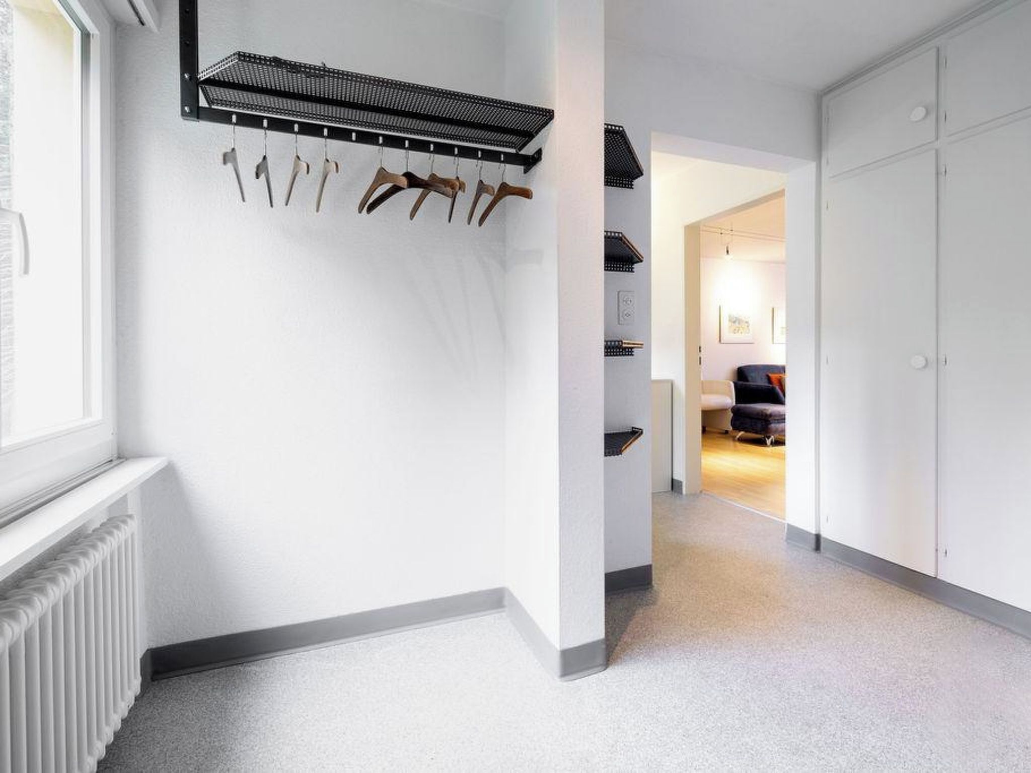 Een gang met een kapstok, een radiator en een deur naar een andere kamer.
