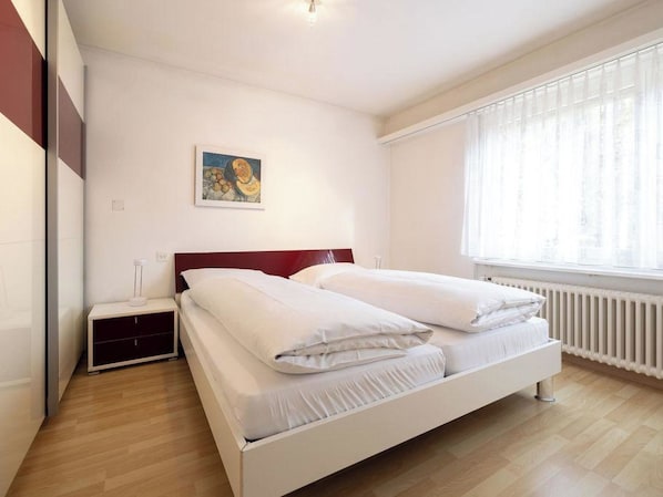 Ein Schlafzimmer mit Bett, Nachttisch, einem Gemälde und einem Fenster mit Vorhängen.