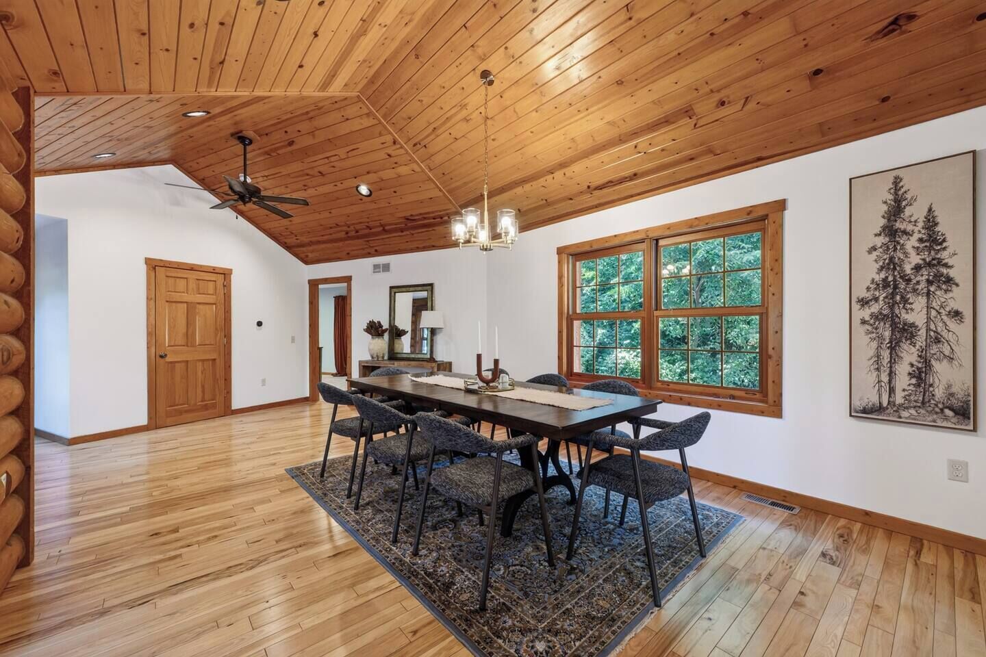 A dining area with a wooden ceiling, large windows, and a table with chairs.