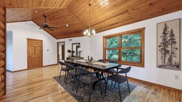 A dining area with a wooden ceiling, large windows, and a table with chairs.