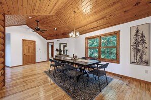 A dining area with a wooden ceiling, large windows, and a table with chairs.