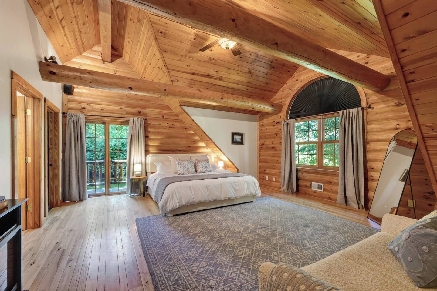 A log cabin bedroom with a bed, a large window, and a view of the outdoors.