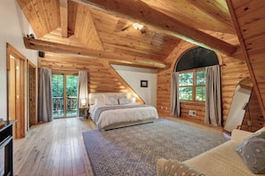 A log cabin bedroom with a bed, a large window, and a view of the outdoors.