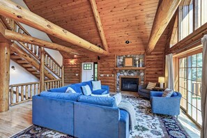 A log cabin interior with a wooden staircase, a fireplace, and a large blue sectional sofa.