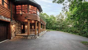 A log cabin with a stone foundation, a wooden porch, and a driveway leading to a garage.