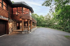 A log cabin with a stone foundation, a wooden porch, and a driveway leading to a garage. - Hickory Hill | Peace + Quiet, Fire Pit, 5 Acres (Wisconsin Dells)