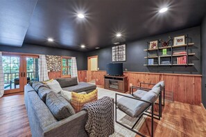 A living room with a sectional sofa, a TV, wooden paneling, and a bookshelf.