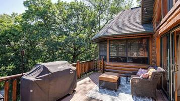 A wooden deck with a covered grill, wicker furniture, and a glass door leading to a room.