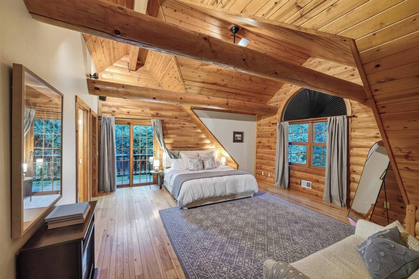 A log cabin bedroom with a bed, a desk, and a large window.