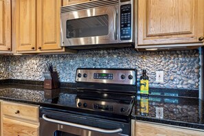 A kitchen with wooden cabinets, a stainless steel microwave, a digital stove, and a granite countertop.