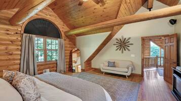 Un dormitorio tipo cabaña de madera con una cama, un sofá, un ventanal grande y un ventilador de techo.