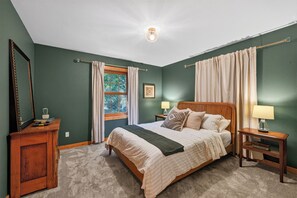 A bedroom with a large bed, two bedside tables with lamps, a dresser, a window with curtains, and a ceiling light.