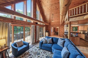 A spacious living area with a blue sofa, a patterned rug, and large windows offering a view of the outdoors.