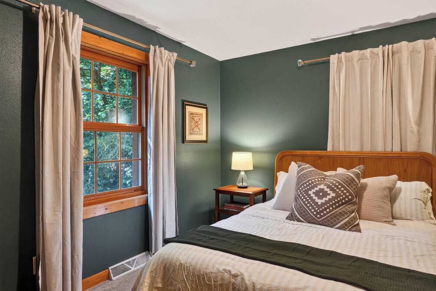 Un dormitorio con cama, mesita de noche, ventana con cortinas y lámpara de pared.
