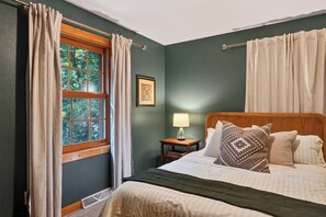 Un dormitorio con cama, mesita de noche, ventana con cortinas y lámpara de pared.