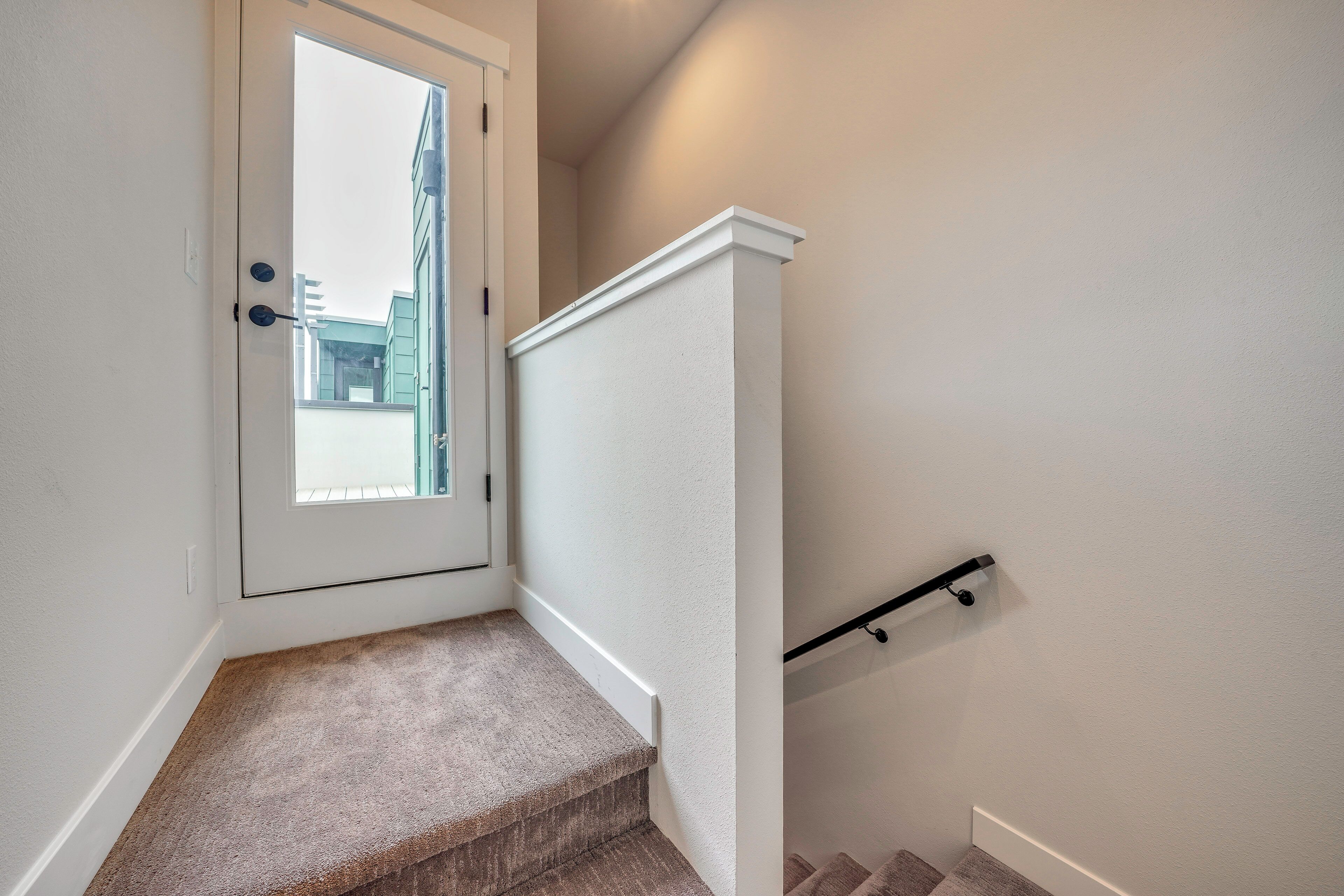 A staircase with a handrail, carpeted steps, and a door leading to an outdoor area.