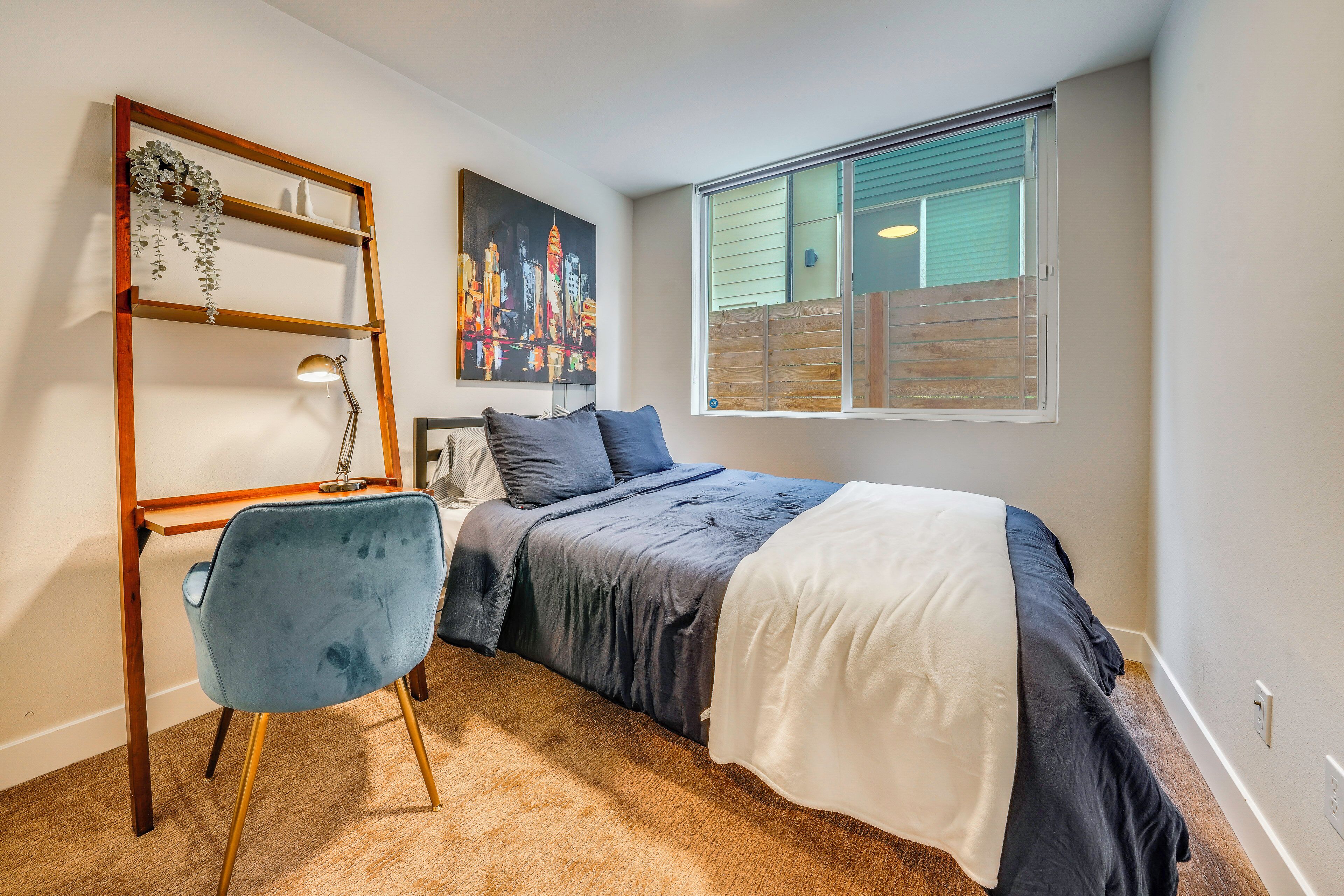 Ein Schlafzimmer mit einem Bett, einem Schreibtisch mit Stuhl, einem Fenster mit Jalousien und einem Stadtbild an der Wand.