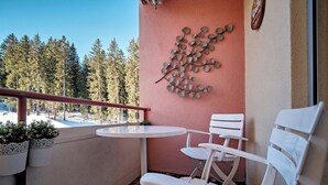 En balkon med et hvidt bord og stole, en dekorativ vægdekoration og udsigt til en sneklædt skov.