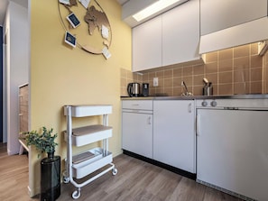 A modern kitchen with a white refrigerator, a coffee maker, and a sink. There is a white cart with shelves and a potted plant. - Paradies 301 Appartement/Fewo, Dusche oder Bad, WC, 4-Bettwohnung by Interhome (Arosa)