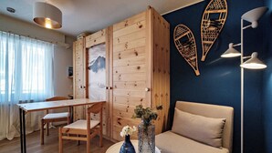 Et hyggeligt værelse med et træskab, et spisebord med stole, en sofa, et rundt bord med en vase og væglamper.