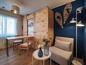A cozy room with a wooden wardrobe, a dining table with chairs, a sofa, a round table with a vase, and wall-mounted lights. - Paradies 301 Appartement/Fewo, Dusche oder Bad, WC, 4-Bettwohnung by Interhome (Arosa)