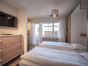 Ein Hotelzimmer mit zwei Betten, einem Fernseher, einem Schminktisch und einem Fenster mit Vorhängen.