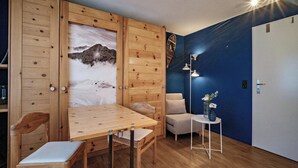Et værelse med et træbord, stole, en sofa, et lille sofabord med en vase, og en væg med et bjergmaleri.