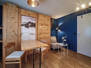A room with a wooden dining table, chairs, a sofa, a small side table with a vase, and a wall with a mountain painting. - Paradies 301 Appartement/Fewo, Dusche oder Bad, WC, 4-Bettwohnung by Interhome (Arosa)
