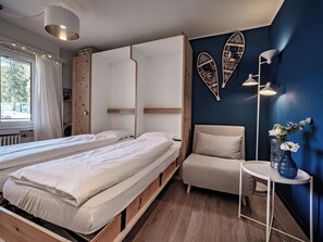 Quarto com duas camas de madeira, uma cadeira, uma mesinha e detalhes decorativos nas paredes.