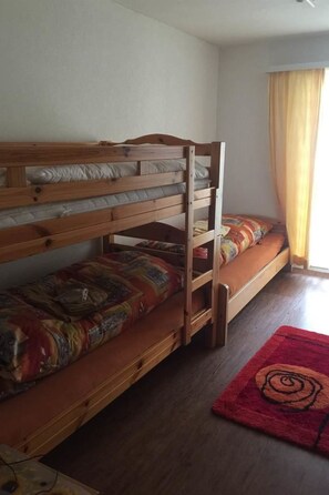 A bunk bed with a wooden frame, a lower bed with a patterned blanket, and a red rug with a spiral design. - Sunnybank / 3. St. Appartement/Fewo, Dusche und Bad, WC, 10-Bettwohnung by Interhome (Arosa)