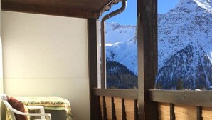 Ein Zimmer mit Blick auf schneebedeckte Berge, einer Holzbalkendecke und einem weißen Sessel mit Kissen.