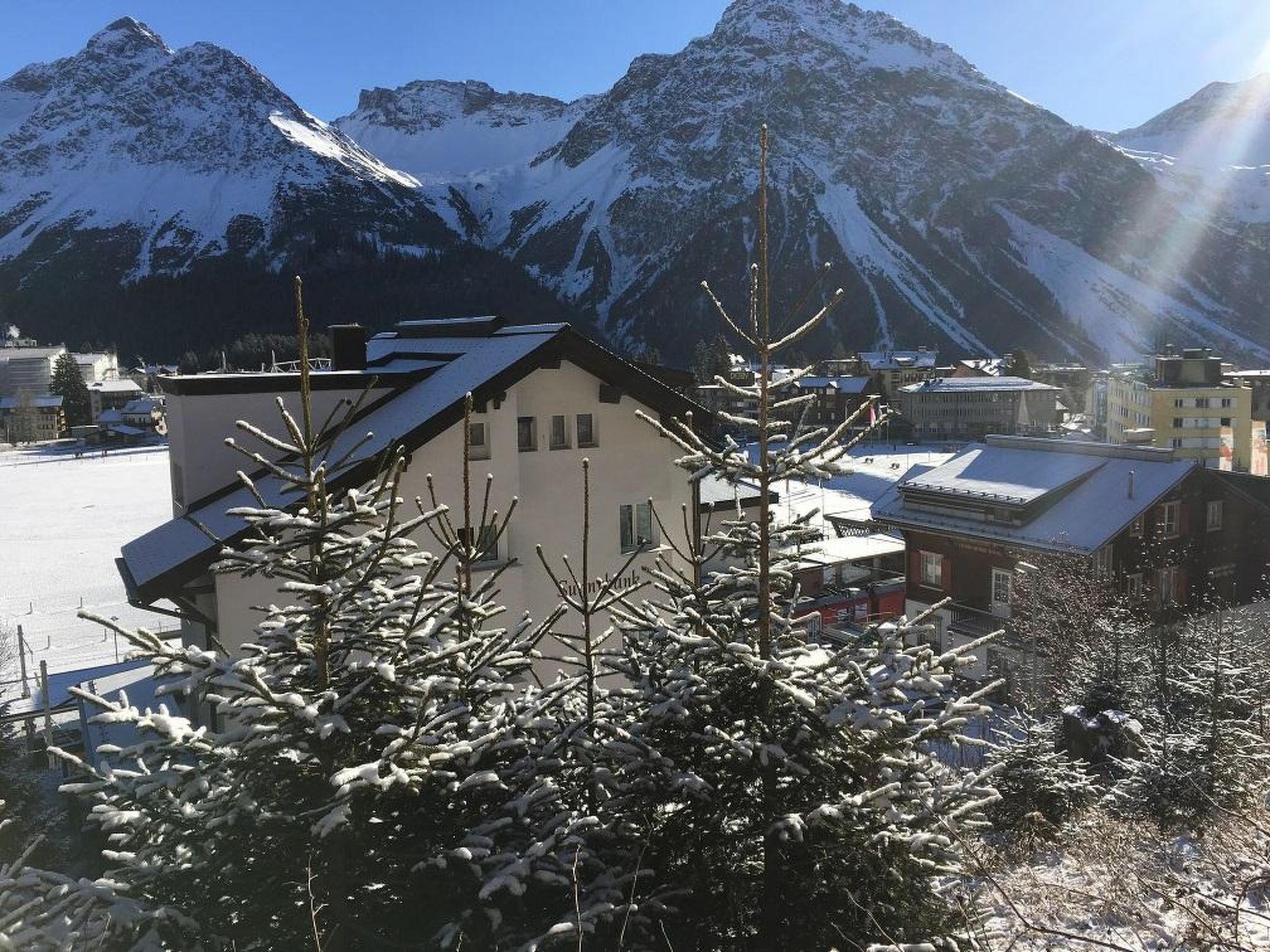 A building with a sloped roof, surrounded by snow-covered trees and mountains in the background.
