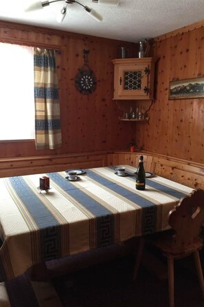 Un coin repas avec une table dressée pour deux personnes, une horloge au mur et une fenêtre avec des rideaux.