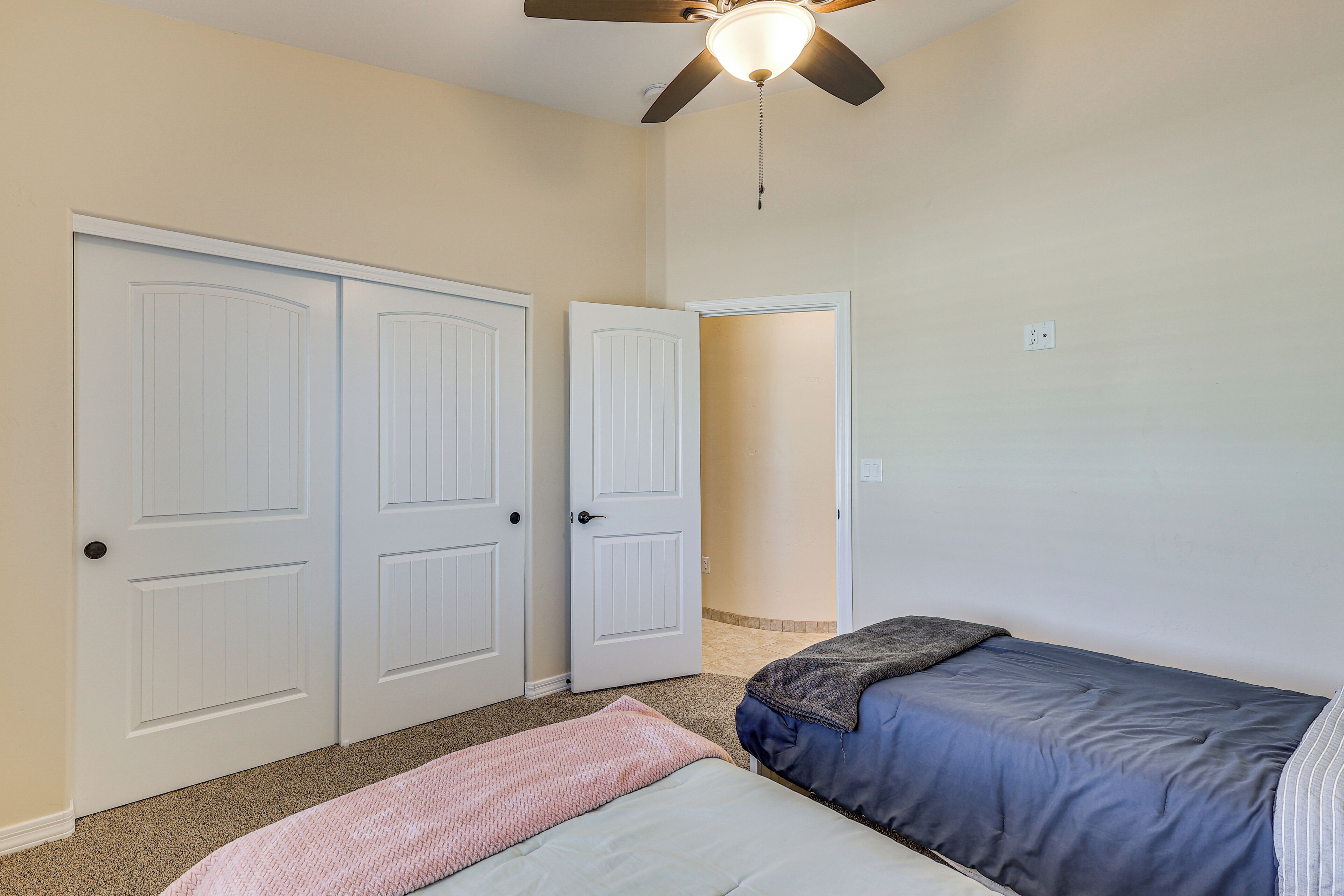 Un dormitorio con dos camas, un ventilador de techo y una puerta que da a otra habitación.