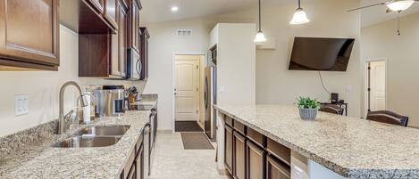 A kitchen with granite countertops, stainless steel appliances, wooden cabinets, and pendant lighting.
