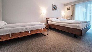 Habitación de hotel con dos camas individuales, un radiador, una ventana con cortinas y un aplique de pared.