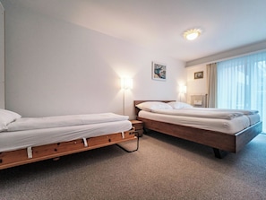 A hotel room with two single beds, a radiator, a window with curtains, and a wall-mounted light fixture. - Paradies 012 Appartement/Fewo,  , 3-Bettwohnung 3-Bettwohnung by Interhome (Arosa)