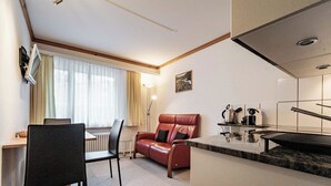 Un espacio habitable compacto con kitchenette, una zona de comedor con mesa y sillas, y un rincón de estar con sofá.